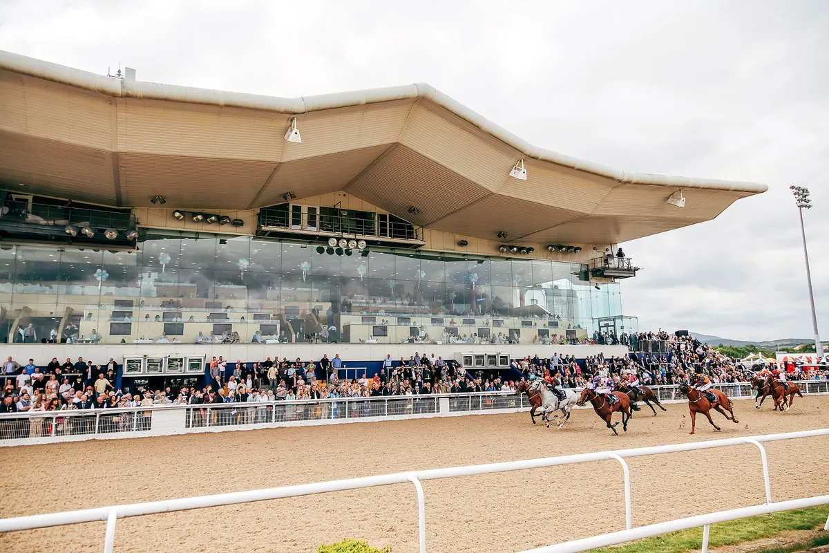Horses racing past a packed grandstand