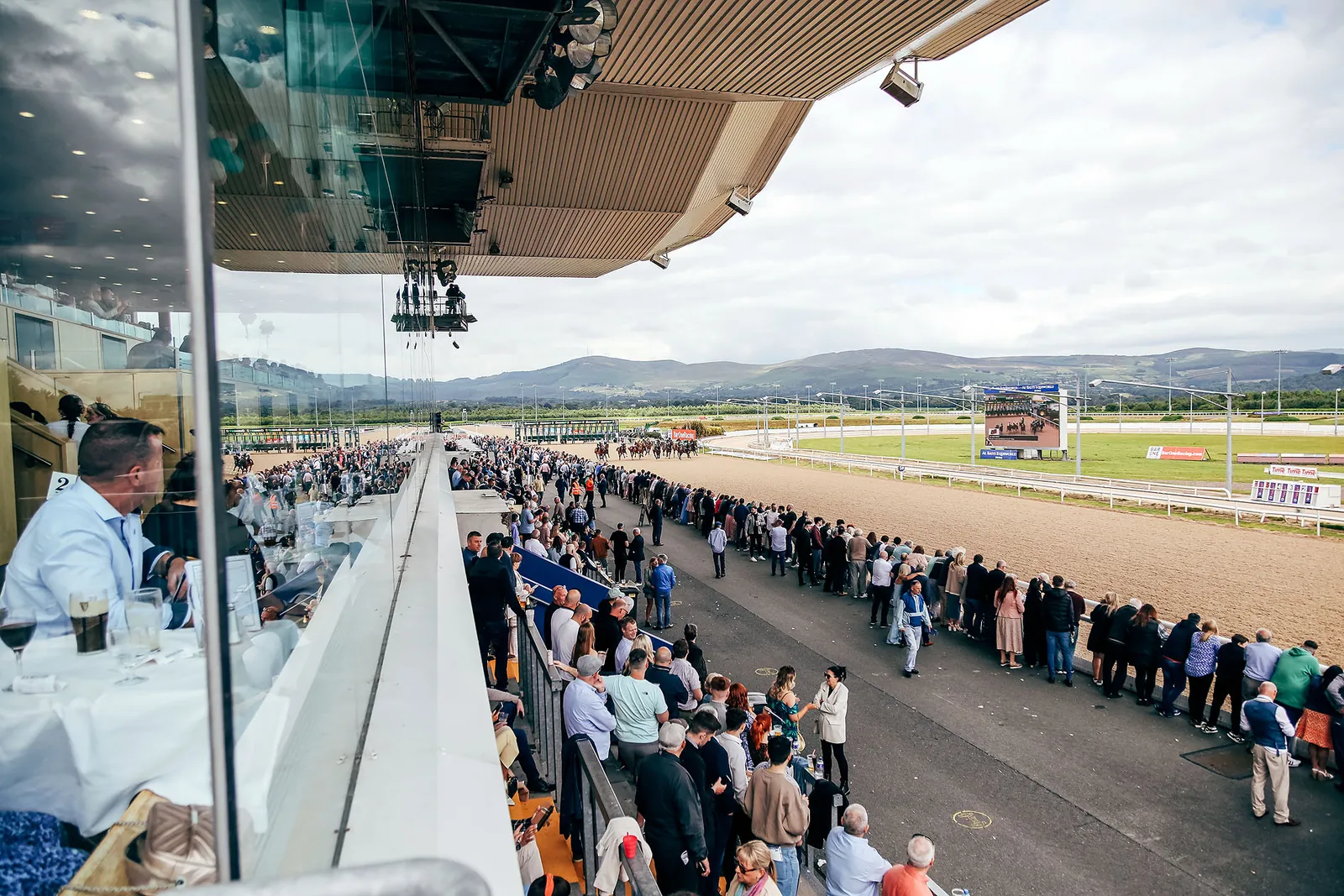 Diners at the long glass wall of The View Restaurant, the track and crowd below