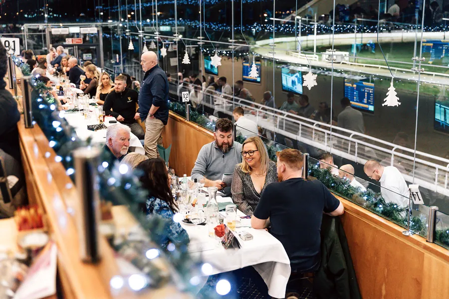 Diners by the glass with the greyhound track lit below